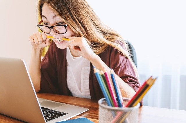 Girl Biting A Pencil In Front Of Laptop
